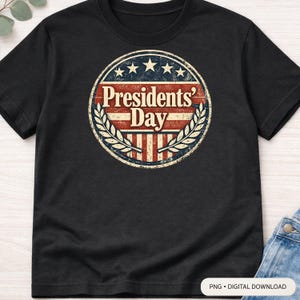 Op de afbeelding: Zwart T-shirt met een cirkelvormig ontwerp. Het ontwerp toont de tekst "Presidents' Day" in rood en wit, omringd door sterren en laurierbladeren. Het ontwerp heeft een vintage look.