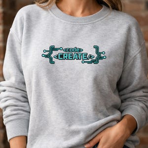 May include: A light gray sweatshirt with the words "<code>CREATE</code>" in a teal circuit board design. The text is centered on the chest. The sweatshirt has a crew neck and long sleeves.