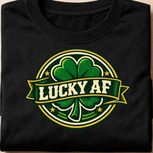 Könnte beinhalten: Schwarzes T-Shirt mit einem kreisförmigen Design, das ein grünes Kleeblatt und den weißen Text "LUCKY AF" zeigt. Das Design hat einen gelben Rand und Sterne und erzeugt einen festlichen Look. Das T-Shirt ist aus weichem Material.