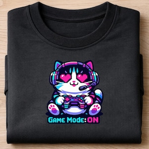 Op de afbeelding: Zwart sweatshirt met een cartoonkat met een koptelefoon en een gamecontroller. De kat heeft hartvormige ogen en de tekst "GAME MODE: ON" in pixellettertype.