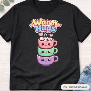 May include: Black t-shirt featuring a stack of three cartoon coffee cups in pink, green, and purple, each with a smiling face. The top cup has marshmallows. Above the cups is the text "Warm Hugs" in a colorful design.