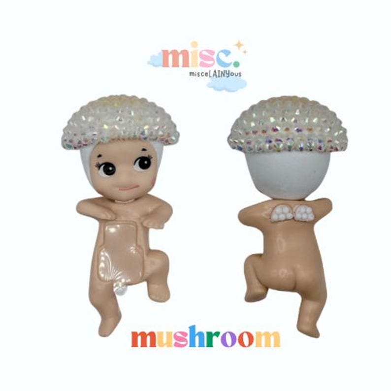 Puede incluir: Dos figuras con tem&aacute;tica de setas. Cada figura tiene una cabeza blanca con adornos iridiscentes y un cuerpo bronceado. Las figuras est&aacute;n en una pose juguetona. La palabra "mushroom" est&aacute; escrita en letras coloridas en la parte inferior de la imagen.