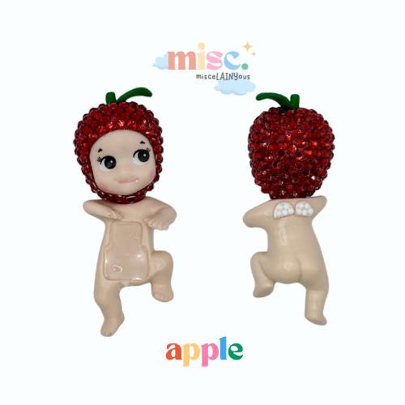 Puede incluir: Dos figuras de un personaje parecido a un beb&eacute; con sombreros rojos brillantes en forma de manzana y tallos verdes. Las figuras tienen un tono de piel claro y est&aacute;n arrodilladas. La palabra "apple" est&aacute; escrita en colores.