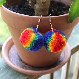 May include: Rainbow pom-pom earrings with silver hooks. The pom-poms are made of yarn and are about 2 inches in diameter.
