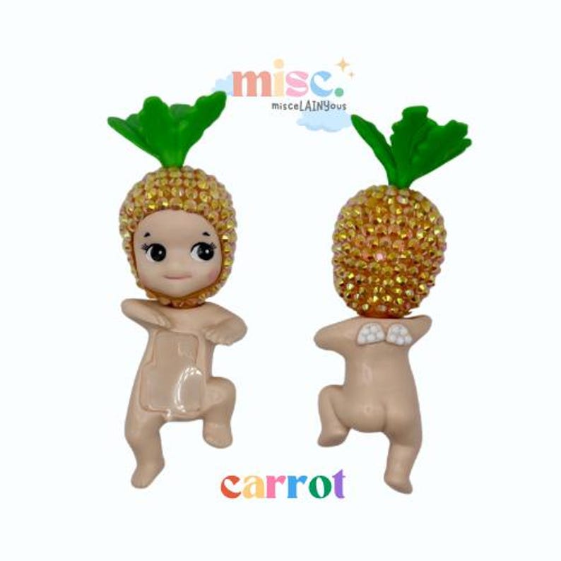 Puede incluir: Dos peque&ntilde;as figuras de color beige, cada una con una cabeza en forma de pi&ntilde;a cubierta de pedrer&iacute;a dorada y hojas verdes. La palabra "carrot" est&aacute; escrita en letras coloridas en la parte inferior. Las figuras est&aacute;n en una pose juguetona.