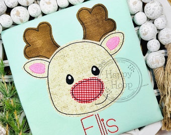 May include: A light blue t-shirt with an embroidered reindeer design. The reindeer has brown antlers, a brown face, a red and white checkered nose, and pink ears. The name "Ellis" is embroidered in red below the reindeer. The text "Stitched by: Simply Sweet Stitches" is embroidered at the bottom of the shirt.