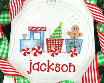 May include: A white onesie with a red, blue, and green Christmas train applique. The train has a gingerbread man, a Christmas tree, and candy cane wheels. The onesie is personalized with the name "jackson" in red.