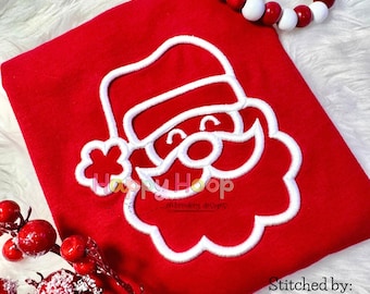 Op de afbeelding: Een rood stoffen item met een wit geborduurd Sinterklaasgezicht. Het Sinterklaasontwerp bevat een hoed, baard en lachend gezicht. De tekst "Happy Hoop" en "Stitched by: American Mom Creations" zijn ook zichtbaar.
