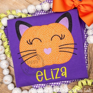 May include: Purple shirt with a black and orange pumpkin cat face applique and the name "Eliza" embroidered in yellow.