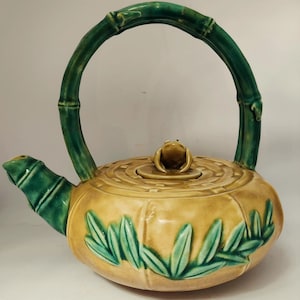 May include: A green and yellow ceramic teapot with a bamboo handle and a frog-shaped lid. The teapot is decorated with green leaves and a bamboo pattern.