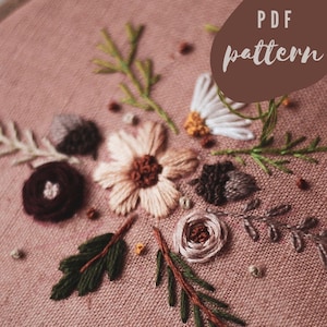 以下が含まれることがあります： ピンクの背景に刺繍された花のフープアート。デザインは、緑、茶色、白、ピンクの色合いのさまざまな花、葉、ベリーを特徴としています。右上の隅に「PDF pattern」というテキストが表示されています。
