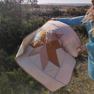 May include: A pink and brown quilt with a star design. The quilt is being held by a person in a blue jacket.