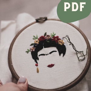 Op de afbeelding: Borduurwerk in een hoepel met een zwart-wit portret van een vrouw met een rode lip en een bloemenkrans. De bloemen zijn rood, roze, geel en blauw.