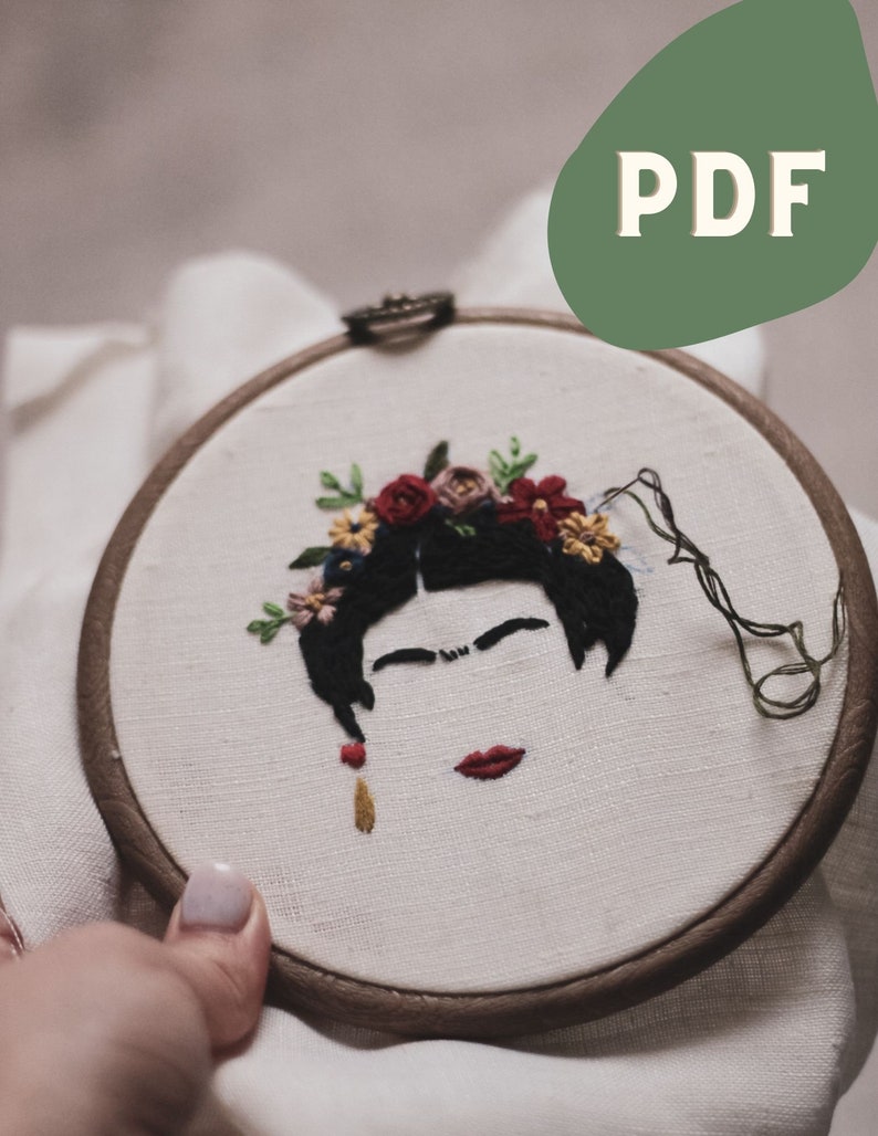 Op de afbeelding: Borduurwerk in een hoepel met een zwart-wit portret van een vrouw met een rode lip en een bloemenkrans. De bloemen zijn rood, roze, geel en blauw.
