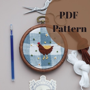 May include: A PDF pattern for a cross-stitch embroidery project featuring a brown chicken with a red comb and yellow feet on a blue and white gingham background. The pattern includes a wooden embroidery hoop, floss, and a needle.