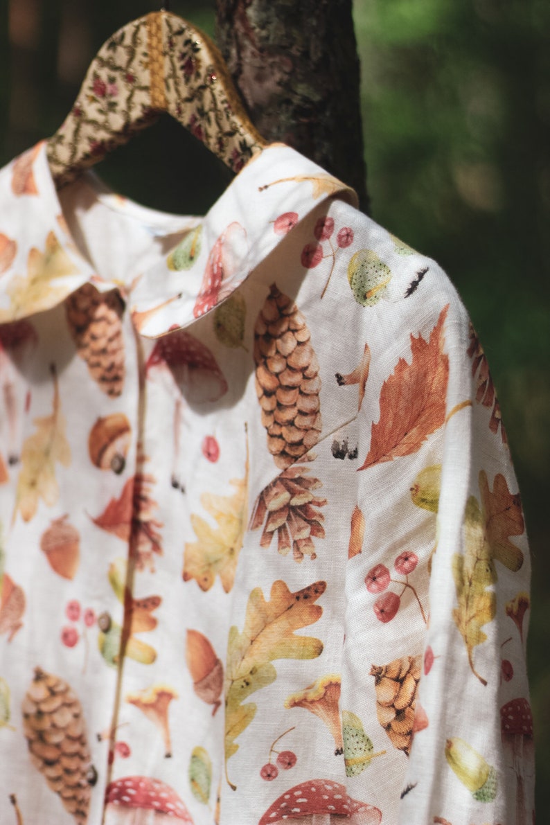 Puede incluir: Una camisa de lino blanca con un estampado de oto&ntilde;o que incluye setas, bellotas, hojas y pi&ntilde;as.