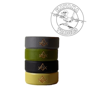 May include: Four stacked silicone rings in gray, olive green, black, and yellow. Each ring features a gold-colored Masonic symbol. The rings are stacked against a white background, with a "Havana Traders" logo in the upper right corner.