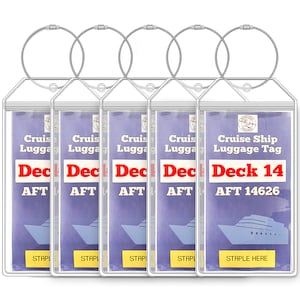 May include: Set of five clear plastic luggage tags with silver metal rings. Each tag has a blue background with white text that reads "Cruise Ship Luggage Tag" and "Deck 14 AFT 14626". The tags have a yellow rectangle at the bottom that says "STAPLE HERE".