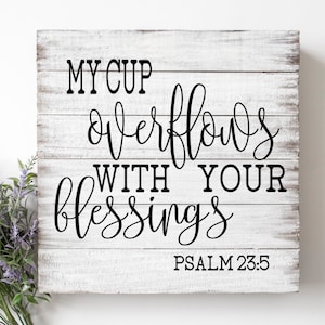 May include: White wooden sign with black lettering that reads "My cup overflows with your blessings Psalm 23:5".
