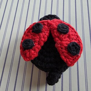 May include: A handmade crochet ladybug with a red body and black spots. The ladybug's head and underside are black. The wings are open, showcasing the detailed crochet work. This whimsical item is likely a decorative piece or a toy.