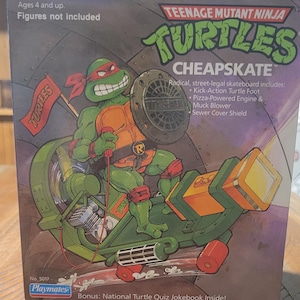 May include: Teenage Mutant Ninja Turtles Cheapskate toy box. The box features a green turtle character riding a green and orange skateboard. The box includes the text "Radical, street-legal skateboard includes: Kick-Action Turtle Foot, Pizza-Powered Engine & Muck Blower, Sewer Cover Shield."