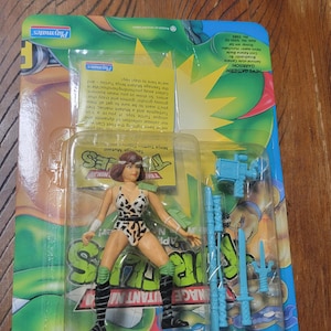 May include: A Teenage Mutant Ninja Turtles action figure, packaged in a clear plastic blister pack. The figure is a female character in a leopard print outfit, with accessories. The packaging has a green and blue design.