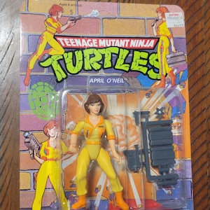 May include: A Teenage Mutant Ninja Turtles April O'Neil action figure in its original packaging. The figure is wearing a yellow jumpsuit and comes with accessories. The packaging features cartoon illustrations of the character and the text "April O'Neil".
