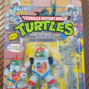 May include: Teenage Mutant Ninja Turtles Raph the Space Cadet action figure, new in package. The figure is wearing a space suit and helmet, with accessories including a space sword and gun. The packaging is yellow and purple.
