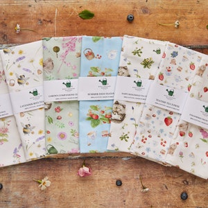 May include: Seven patterned tea towels with floral and animal motifs, including bees, lavender, and strawberries. Each towel has a unique design and is labelled with the text "West Country Designs" and a tea-related name. Made in Britain.