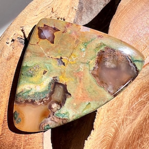 May include: A white ceramic mug with a black handle and the text "But First, Coffee" in a bold, black font. The mug is set against a blurred background, suggesting a cozy setting.