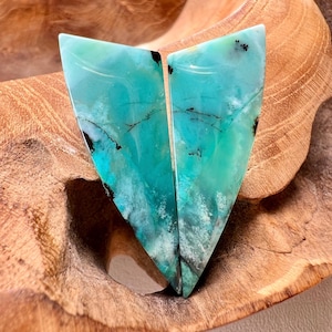 May include: Two triangular polished gemstones featuring a vibrant turquoise and teal color palette with intricate black dendritic inclusions and white cloudy patterns. The stones have a smooth, glossy surface and are shaped into matching geometric forms.