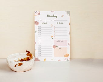 May include: A daily planner sheet titled Monday with a schedule from 06:00 to 20:00, a to-do list, a goal for today box, and a notes section. The paper features pastel floral and rainbow illustrations in pink, orange, and green on a white background.