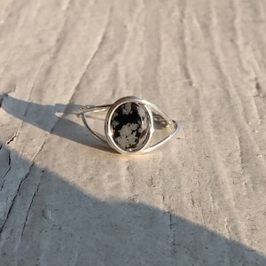 May include: A silver ring with a black and white snowflake obsidian stone set in an oval shape.