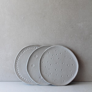 May include: Three gray ceramic plates with unique textures. One plate features a dotted border, another has a crescent moon design, and the third is covered in small, evenly spaced dots. The plates are round and have a minimalist aesthetic.