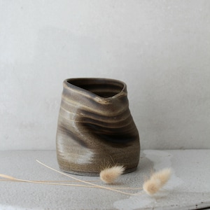 May include: A brown ceramic vase with a wavy, organic shape. The vase has a light brown glaze with darker brown streaks.