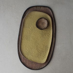 以下が含まれることがあります： 薄い茶色、黄色、濃い茶色のカラーリングのセラミック製サービングディッシュ2点セット。大きな皿は楕円形で、小さな皿は丸い。両方の皿は表面がテクスチャ加工されている。