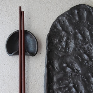 May include: Black ceramic chopstick rest and a matching plate with a textured surface.