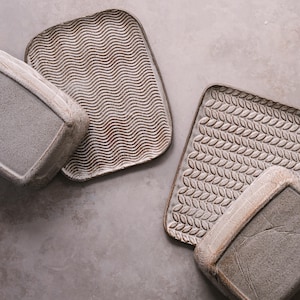 Könnte beinhalten: Vier Keramik-Servierplatten mit verschiedenen Texturmustern. Die Platten sind in Grautönen und Braun.