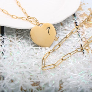 May include: A gold heart-shaped pendant necklace with a number 7 engraved on the front. The necklace is made of a delicate chain.