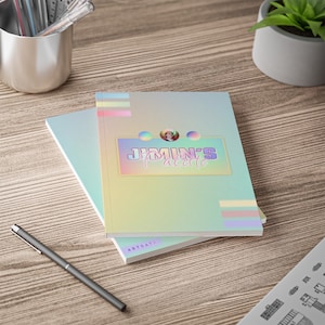 May include: Two notebooks with a holographic iridescent cover. The top notebook has the text "Jimin's Palette" in a colorful font. The bottom notebook has the text "Artsata" printed on the cover.