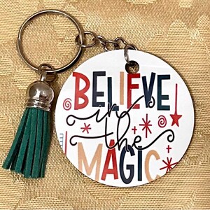 May include: A white round keychain with the text "Believe in the Magic" in colorful letters and a green tassel.