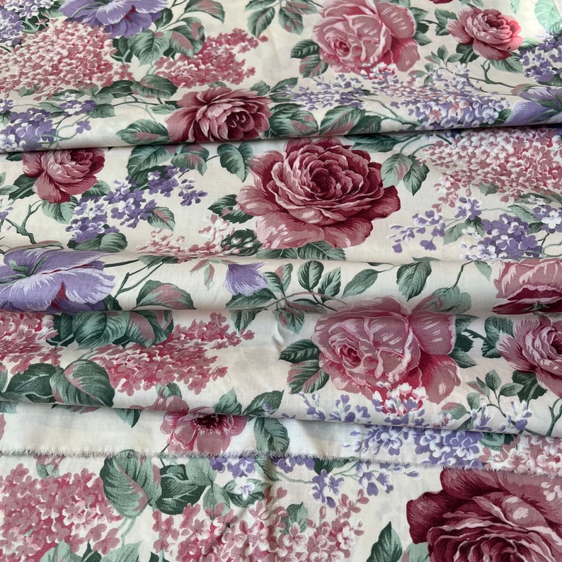 Pode incluir: Um tecido branco com um padr&atilde;o floral com flores rosa e roxas. O tecido tem uma superf&iacute;cie texturizada e um brilho sutil.
