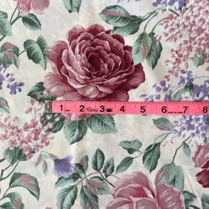 Pode incluir: Um tecido branco com um padr&atilde;o floral com rosas cor-de-rosa e flores roxas. Uma fita m&eacute;trica rosa &eacute; colocada sobre o tecido, mostrando 8 polegadas.
