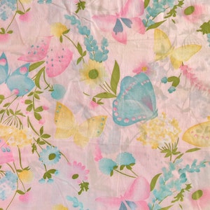 May include: A pink fabric with a repeating pattern of butterflies and flowers. The butterflies are in shades of pink, blue, and yellow. The flowers are in shades of pink, blue, and yellow.