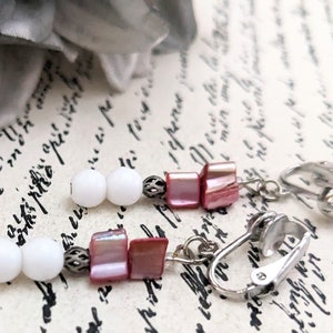 May include: A pair of clip-on earrings with white beads and pink shell-like pieces. The earrings have silver-toned metal accents.