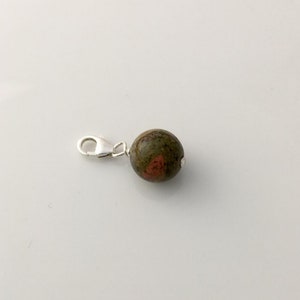 May include: A silver charm with a round, green and red jasper bead.