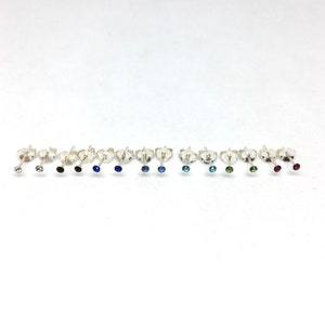 May include: A set of 10 pairs of silver stud earrings with different coloured gemstones. The gemstones are clear, black, blue, light blue, dark blue, green, and red.