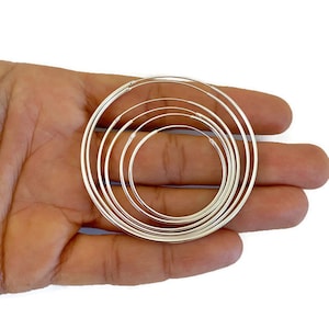 May include: A set of six silver hoop earrings of varying sizes. The hoops are arranged in a nested pattern, with the largest hoop at the top and the smallest hoop at the bottom.