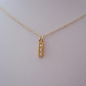 May include: A gold chain necklace with a small pendant featuring three clear stones set in a vertical bar.