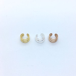 May include: Three ear cuffs in gold, silver, and rose gold. Each cuff is made of three thin, curved bands.